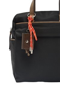 Czarna torba materiałowa z brązowymi skórzanymi akcentami, z czerwono-białym plecionym pendansem i małym brązowym portfelem przymocowanym.