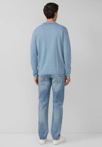 Jasnoniebieski sweter w paski z okrągłym dekoltem, długimi rękawami i prążkowanymi mankietami, zestawiony z jasnoniebieskimi jeansami i białymi tenisówkami.