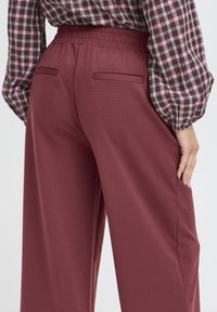 Pantaloni largi de culoare bordo cu talie elastică, având două buzunare la spate și o textură fină. Asortați cu o bluză cu model în carouri.