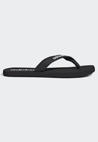Chancla negra con suela texturizada, que presenta una correa elegante y un atrevido logo blanco en la parte superior. Diseño ligero para uso casual.