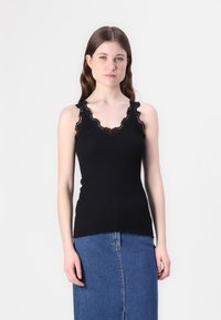 Svart ribbestrikket tanktopp med bølget blondekant ved halsen og skulderstroppene. Figursydd design, kombinert med et denimskjørt.
