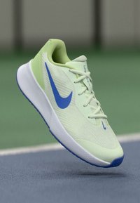 Hellegrüner Sportschuh mit strukturiertem Obermaterial, blauem Nike-Swoosh und weißer Sohle. Verfügt über Schnürsenkel und ein gepolstertes Design für Unterstützung.