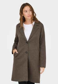 Bruin wollen blend jas met een ingesneden kraag, enkele knoopsluiting, voorkiezen en een rechte snit. Gecombineerd met een witte top.
