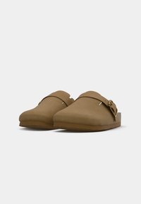 Brown suede slip-on clogs with adjustable buckle straps and flat rubber soles, shown against a plain white background.