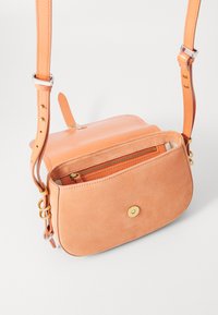 Borsa a tracolla in pelle pesca con texture scamosciata, tasca frontale con zip, hardware dorato e tracolla regolabile. Forma rettangolare con bordi arrotondati.