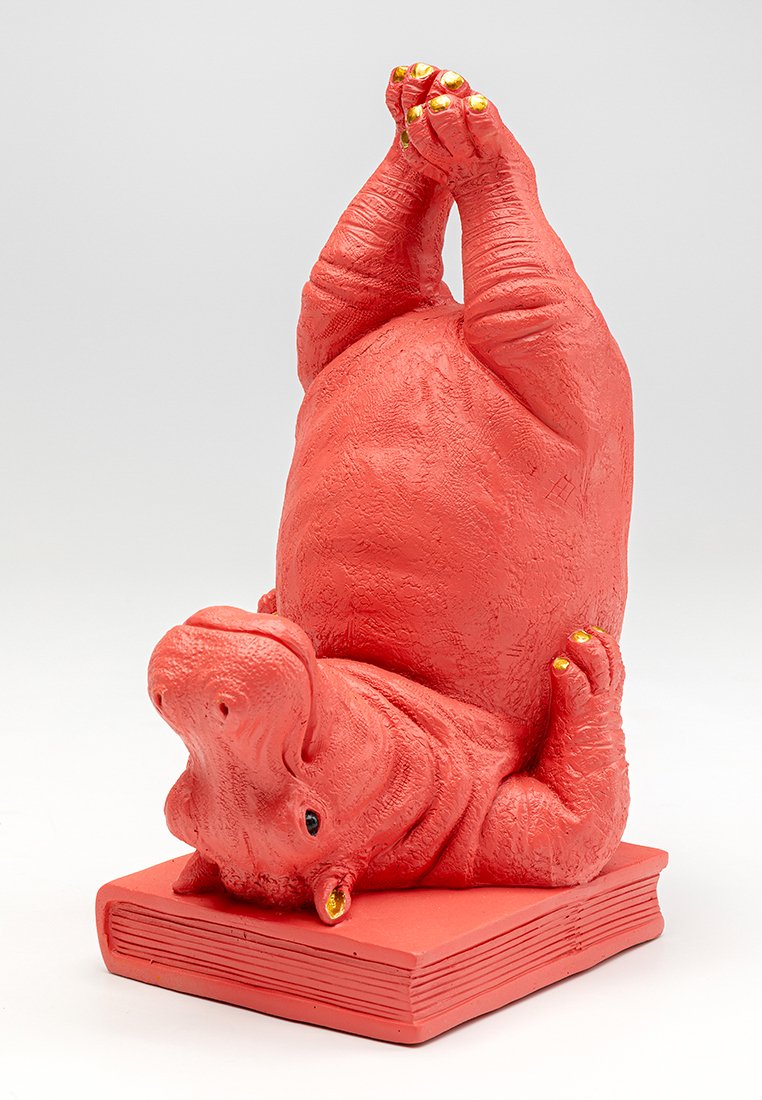 Rote Nilpferdfigur, kopfüber auf einem roten Buch positioniert, mit strukturiertem Fell und goldverzierten Klauen und Augen.