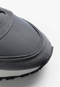 Grauer Sportschuh mit einem Obermaterial aus Mesh und Akzenten aus Wildleder. Abgerundete Zehenpartie, kontrastierende weiße Zwischensohle und strukturierte Gummisohle.