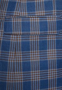 Niebieska tkanina w kratę z wzorem brązowych i jasnoniebieskich linii przecinających się, o gładkiej fakturze i z jednym detalem w postaci kieszonki.