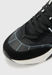 Black sneaker with textured suede and synthetic upper. Features gray accents, flat laces, and a cushioned white sole.