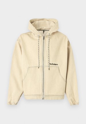 Sweat à capuche beige zippé avec poches avant, cordons noirs et blancs et texte brodé "No Problemo" sur la poitrine gauche.