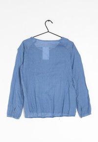 Blusa azzurra chiara con pois bianchi, maniche lunghe, polsini elastici e scollatura rotonda. Realizzata in un tessuto leggero e trasparente.