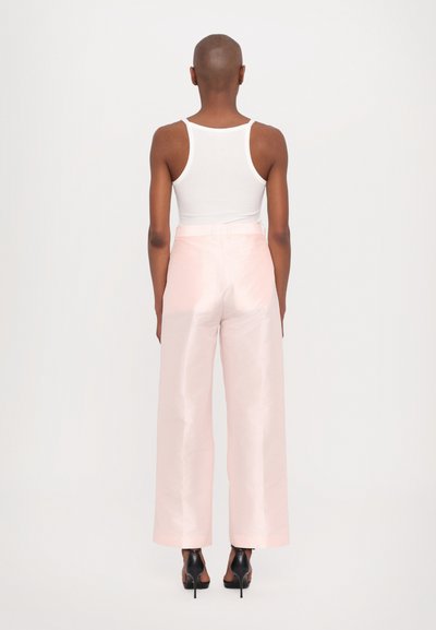 Pink, wide-leg trousers made of a shiny fabric, featuring a high waist and belt loops, paired with a white tank top and black heeled shoes.
