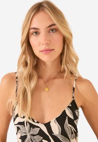 Abito nero e crema con motivi floreali, caratterizzato da spalline sottili e scollatura a V. Una collana con pendente d'oro è visibile.