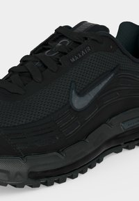 Μαύρο αθλητικό παπούτσι Nike Max Air με επάνω μέρος από δίχτυ, κλείσιμο με κορδόνια, υφασμένο πέλμα και χαρακτηριστικό λογότυπο Swoosh στο πλάι.