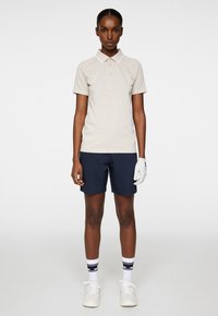 Beige polo shirt med vit krage, parat med marinblå shorts. Vita handskar och skor, randiga marinblå och vita strumpor ger detalj.