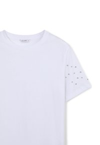 T-shirt bianco con maniche corte e scollatura rotonda. Una manica decorata con borchie argentate di varie dimensioni per texture e dettagli.