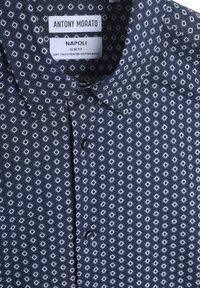 Marineblauwe kortmouwshirt met een slim fit, voorzien van een geometrisch wit diamantenpatroon en een knoopsluiting. Gemaakt van een zacht katoenmix.