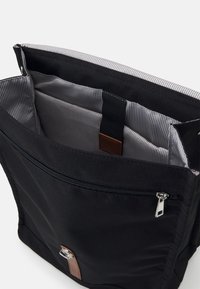 Black fabric messenger bag with a zippered opening, striped interior lining, and a brown leather accent on the front. Multiple interior compartments.