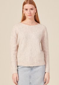 Maglione rosa chiaro con motivo a rovescio, maniche lunghe e scollo ampio. Tessuto morbido e orlo a coste. Indossato con una gonna di jeans.