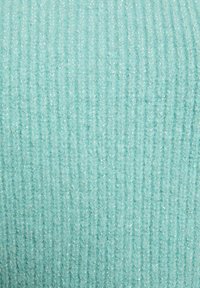 Tessuto a maglia in un morbido verde menta, caratterizzato da una texture a righe verticali. Fili sottili riflettono la luce, aggiungendo una leggera lucentezza alla superficie.