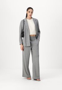 Gray pinstripe suit with wide-leg trousers and a slightly oversized blazer, paired with a white textured crop top and black handbag.