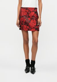 Rød blomstermuster miniskjørt med svart bakgrunn, med en jevn tekstur. Kombinert med svarte spisse sko og svarte ankelstrømper.