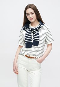 Csíkos rövid ujjú ing fehér és tengerészkék színekben, széles fehér nadrággal párosítva. Egy tengerészkék pulóver lóg a vállakon. Barna öv díszítésként.