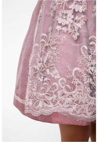 Robe rose courte en tissu texturé avec une broderie florale blanche complexe le long de l'ourlet. Dispose d'une superposition transparente et d'un bord festonné.