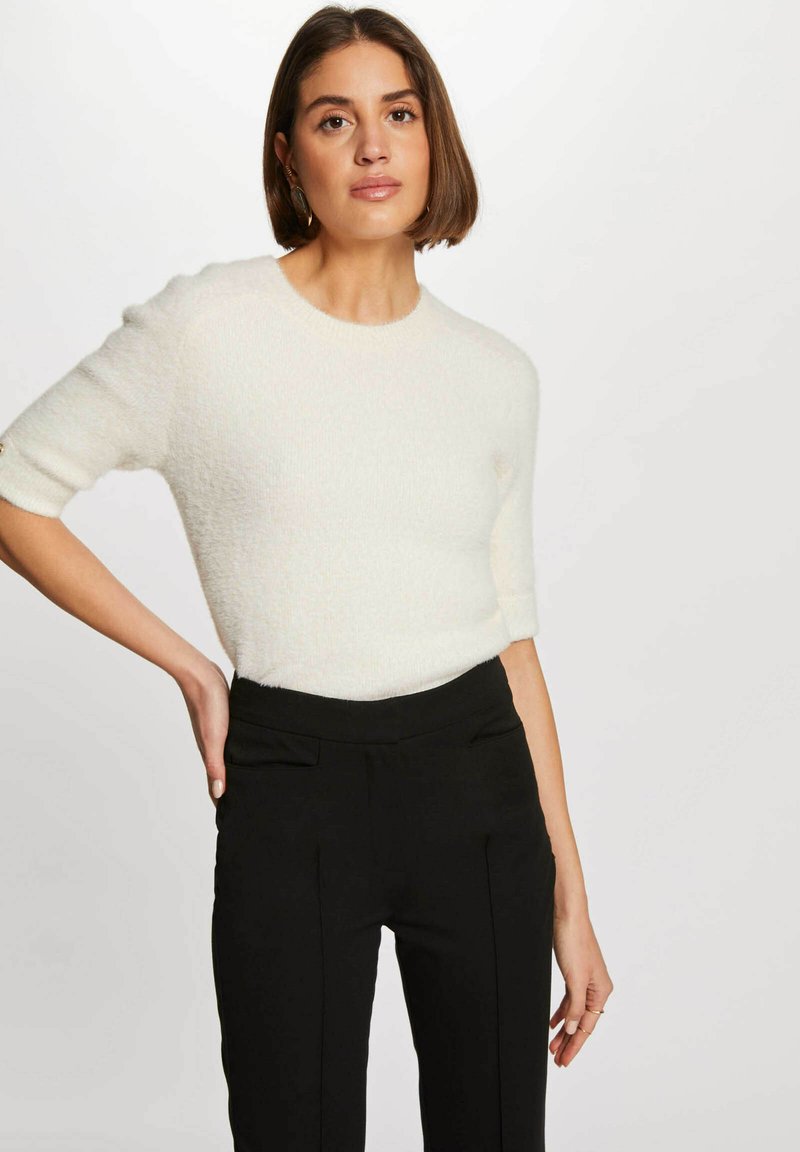 Maglione bianco a maniche corte con lavorazione a maglia testurizzata, scollatura rotonda e design aderente, abbinato a un paio di pantaloni neri su misura con pieghe frontali.