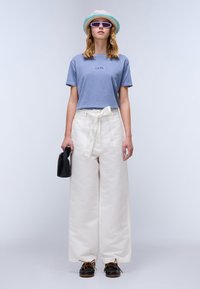 Blauwe katoenen cropped t-shirt met reliëflogo, brede witte hooggewaisting broek met strikriem, zwarte tas en zwarte schoenen met bruine veters.