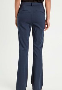 Marineblaue, weit ausgestellte Hosen mit glatter Textur, die flache Taschen und einen taillierten Bund für eine enganliegende Passform aufweisen.