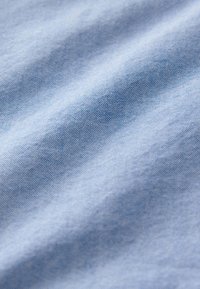 Vaaleansininen kangas, jossa on sileä tekstuuri ja lievä kiilto, sisältäen hienovaraisia värivaihteluita ja tasaisen kudontamallin.