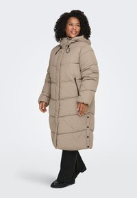 Beige vadderad lång kappa med huva, med horisontell sömnad, sidofickor med dragkedja och knapplist längs fållen.