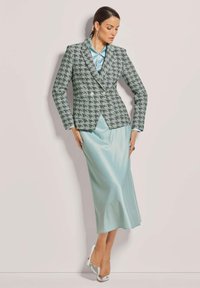 Grüner und weißer gemusterter Blazer mit taillierter Passform, kombiniert mit einem hellblauen Satinkleid und silbernen High-Heels.