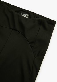 Pantalones cortos deportivos negros con una textura de tela suave, que presentan un diseño de costura curva y una cinturilla elástica. Logo visible en la cinturilla.