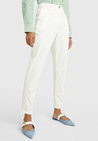 Pantaloni in cotone bianchi con una vestibilità dritta, dotati di pieghe frontali, bottone in vita, abbinati a ballerine a punta a strisce blu e bianche.