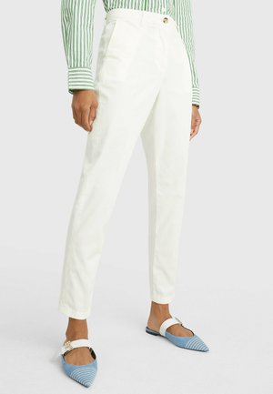Pantaloni in cotone bianchi con una vestibilità dritta, dotati di pieghe frontali, bottone in vita, abbinati a ballerine a punta a strisce blu e bianche.