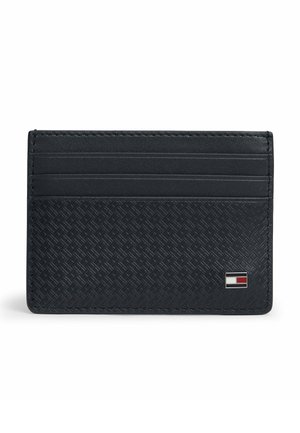 Czarny teksturowany skórzany uchwyt na karty z trzema miejscami na karty oraz małym prostokątnym logo w kolorach czerwonym, białym i granatowym w dolnym prawym rogu.