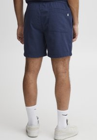 Marineblaue Shorts aus strukturiertem Stoff, mit einem elastischen Bund und einer Gesäßtasche, kombiniert mit weißen Socken und Turnschuhen.