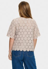 Top in pizzo color beige chiaro con motivo floreale a intagli, maniche corte e orlo scallop. Abbinato a jeans in denim blu a vita alta.