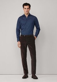 Navyblauw, geruit overhemde met lange mouwen, gecombineerd met bruine, slim-fit corduroy broek. Donkere schoenen maken de outfit compleet.