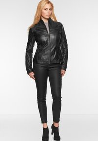 Schwarze Lederjacke mit Reißverschluss, Schulter- und Seitennähten, kombiniert mit figurbetonten schwarzen Hosen und hochhackigen Stiefeletten.