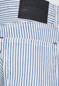 Un bolsillo de jeans de mezclilla a rayas verticales azul y blanco con una etiqueta de cuero negra de la marca Levi's encima que muestra el tamaño W32 L32.