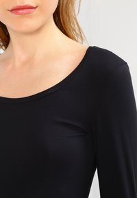 Schwarzes Langarmoberteil mit weitem Rundhalsausschnitt, aus dehnbarem Stoff, mit glatter Textur und taillierter Form an den Schultern.