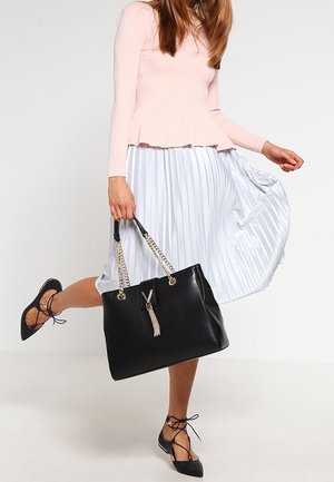 Sac à main en cuir noir avec bretelles en chaîne argentée, détail à pampilles, et forme structurée, assorti à un haut côtelé rose clair et une jupe plissée.