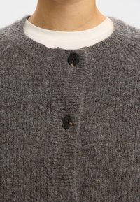 Grijze gebreide cardigan met een textuurpatroon, ronde hals en twee zwarte knopen aan de voorkant. Zachte wol of een vergelijkbaar materiaal.