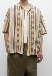 Camicia a maniche corte con bottoni realizzata in tessuto pattern beige, caratterizzata da righe multicolori, motivi a diamante e farfalle, e un colletto pieghevole.