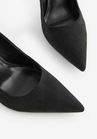 Scarpe con tacco alto in suede nero con design a punta e lati aperti. Fodera interna liscia e superficie opaca all'esterno.