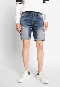 Jeansshorts i urtvättad blått med slitna detaljer. Upprullad fåll och femficksdesign. Kombinerat med en vit ribbad tröja och vita sneakers.