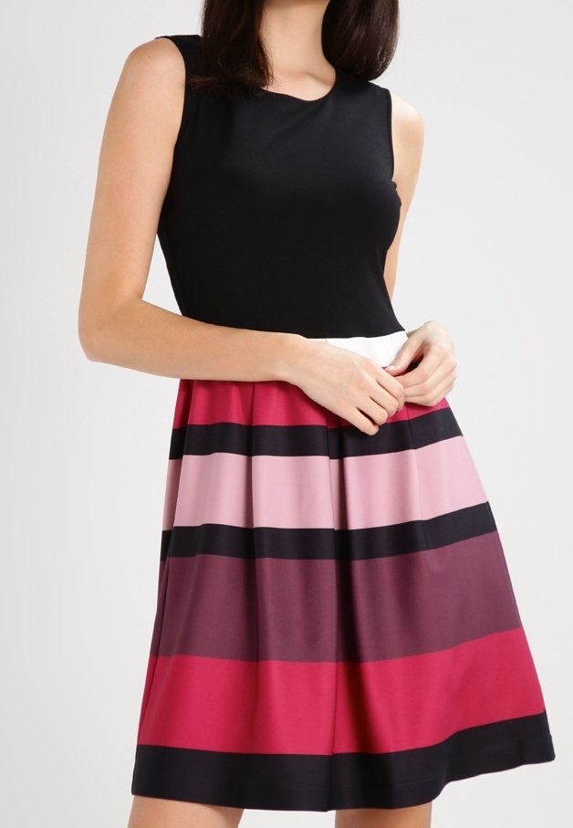 Femme portant un haut noir sans manches et une jupe plissée avec des rayures horizontales rouges, roses, noires et bordeaux.